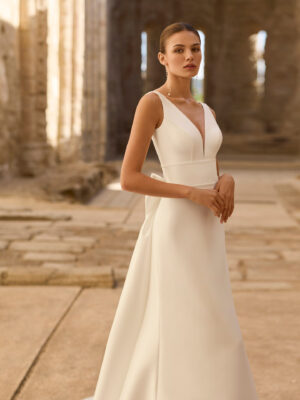 Vestido de novia Princes de Adriana Alier 2027 en crepé con escote en V, mangas largas de gasa, espalda en V con gran lazo y falda de línea A.