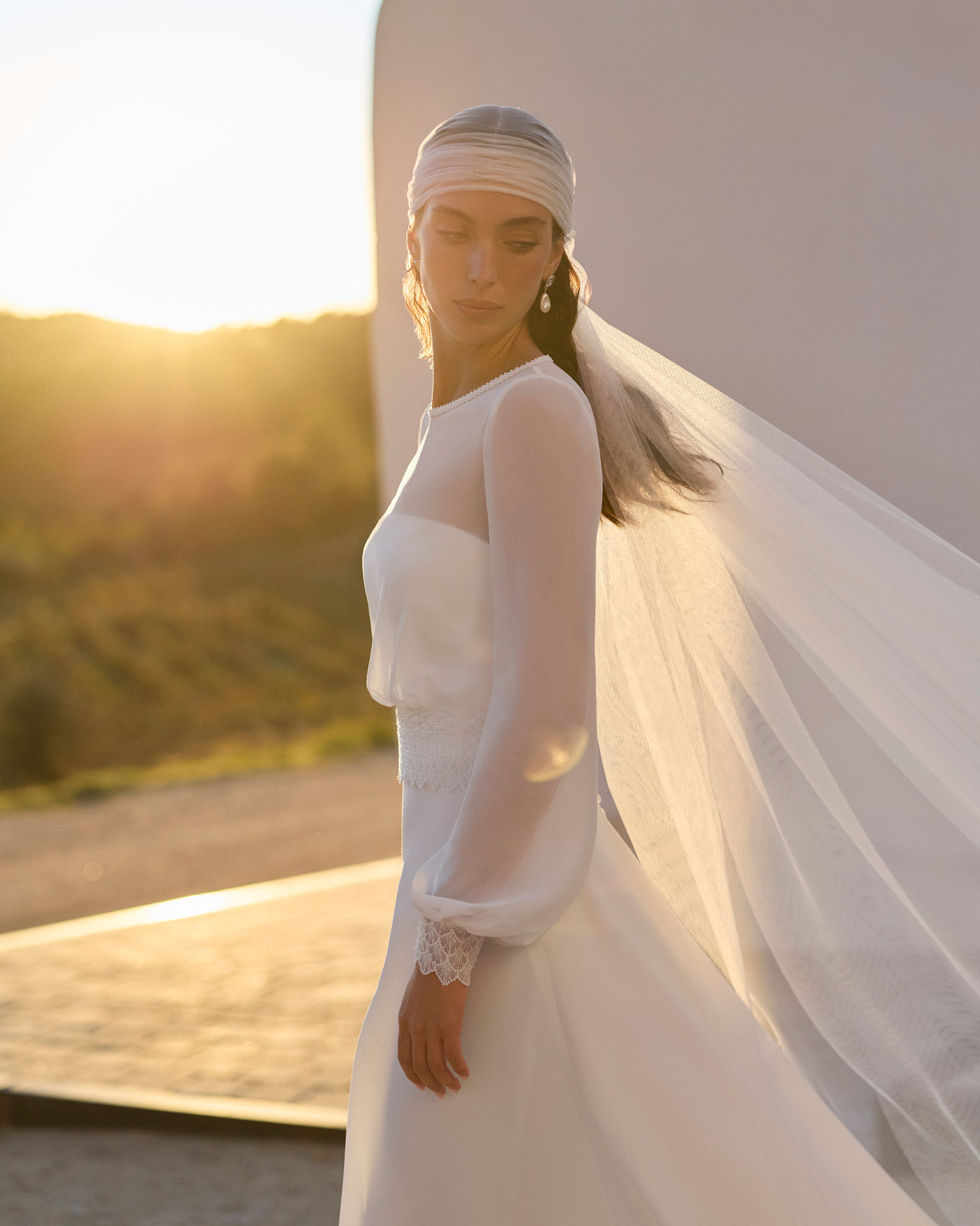 Vestido de novia Relia de Aire Barcelona 2027 con mangas largas de gasa transparente, escote barco, cintura de encaje, falda fluida de crepé y elegante espalda cerrada.