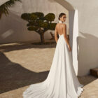 Vestido de novia Renys de Aire Barcelona 2027 en crepé con escote halter, espalda descubierta, cintura bordada y falda de caída fluida.