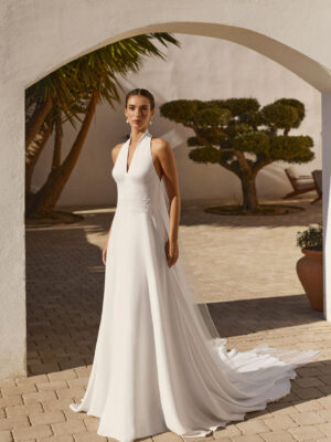 Vestido de novia Renys de Aire Barcelona 2027 en crepé con escote halter, espalda descubierta, cintura bordada y falda de caída fluida.