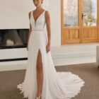 Vestido de novia Riga de Aire Barcelona 2027 de corte A en gasa plisada con escote en pico, espalda en V, abertura frontal y capa de gasa.