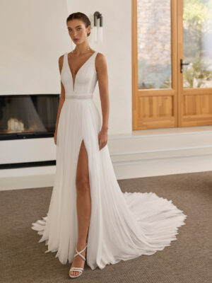 Vestido de novia Riga de Aire Barcelona 2027 de corte A en gasa plisada con escote en pico, espalda en V, abertura frontal y capa de gasa.
