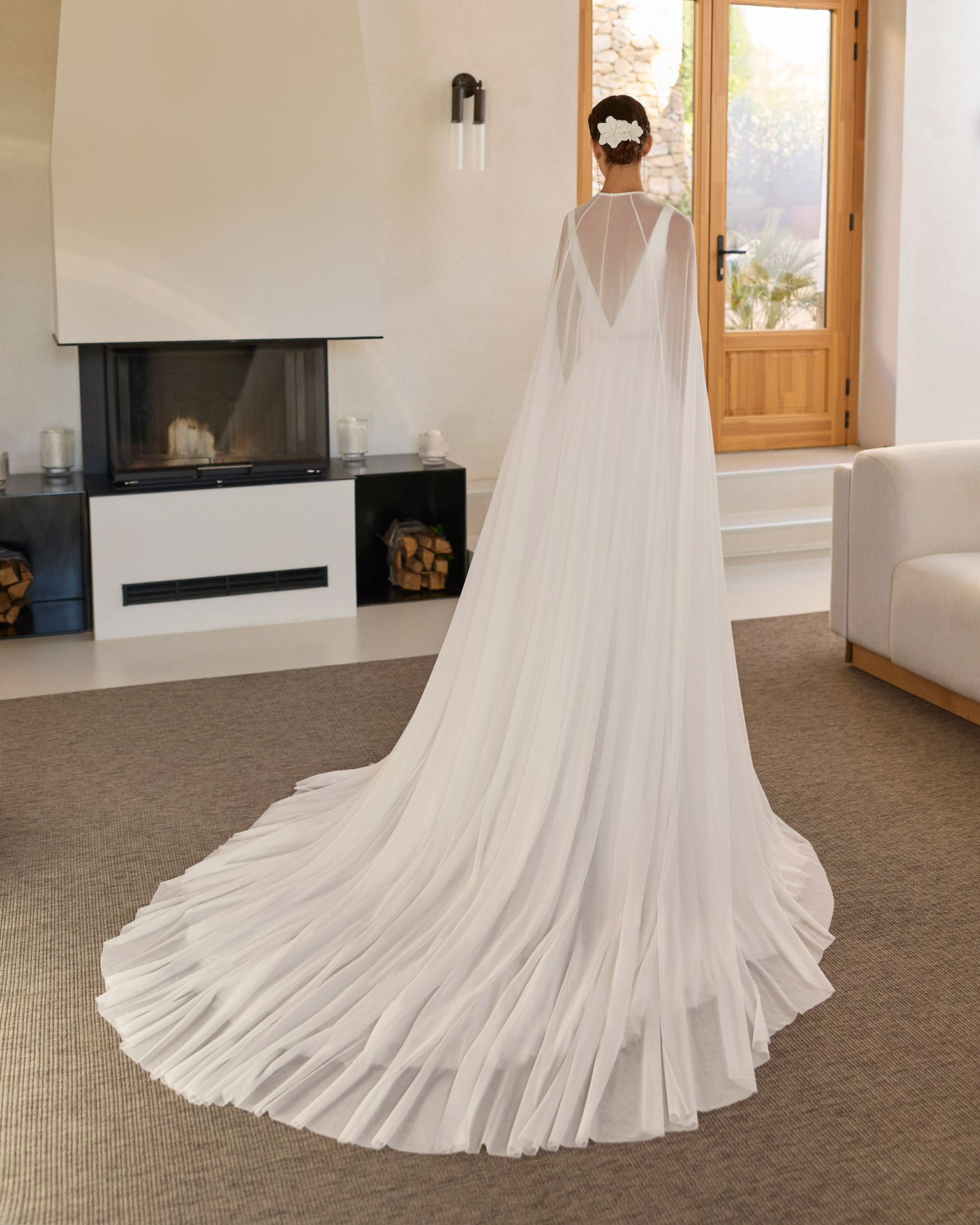 Vestido de novia Riga de Aire Barcelona 2027 de corte A en gasa plisada con escote en pico, espalda en V, abertura frontal y capa de gasa.