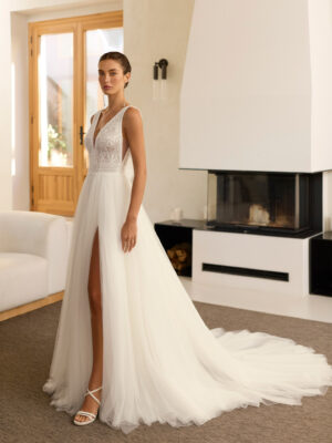 Vestido de novia Riosa de Aire Barcelona 2027 de corte A en tul con escote en pico, cuerpo de encaje floral, espalda en V, abertura frontal y detalle floral en la espalda.