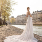 Vestido de novia Tatiana de Aire Barcelona 2027 de línea A con cuerpo de encaje floral, escote caja, espalda abierta con cadenas joya y falda vaporosa con cola de encaje.