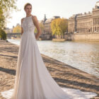 Vestido de novia Tatiana de Aire Barcelona 2027 de línea A con cuerpo de encaje floral, escote caja, espalda abierta con cadenas joya y falda vaporosa con cola de encaje.