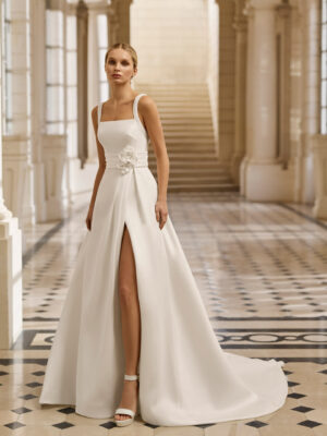 Vestido de novia Aire Barcelona 2027 de mikado con escote cuadrado, tirantes anchos, falda línea A con abertura delantera y detalle floral en la cintura.2