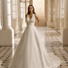 Vestido de novia Aire Barcelona 2027 de mikado con escote pico, cuerpo de encaje floral y falda evasé de estilo clásico y elegante.