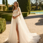 Vestido de novia Xenea de Aire Barcelona 2027 de corte A en tul bordado con escote cuadrado, cuerpo de encaje floral, abertura frontal y capa de tul integrada.