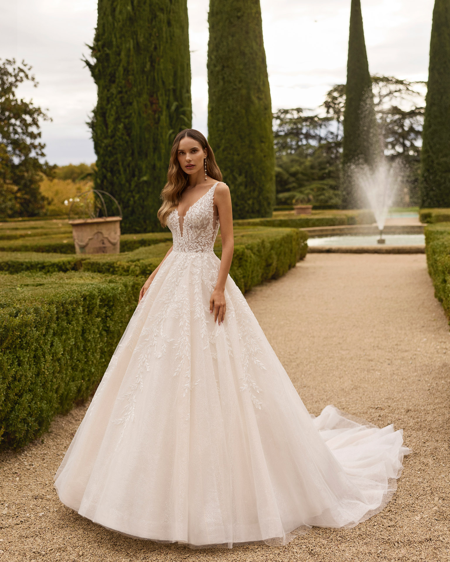 xiona-vestido-novia-princesa-encaje-floral-aire-barcelona-2027.frente Vestido de novia Xiona de Aire Barcelona 2027 de corte princesa con escote en V, cuerpo de encaje floral, espalda descubierta y amplia falda de tul con brillo.